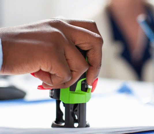 Conta Notarial já está disponível em todo o Brasil: entenda como ela funciona e por que pode facilitar sua vida Tabelião em cartório digital mostrando no tablet o uso da Conta Notarial com casal ao fundo assinando escritura.